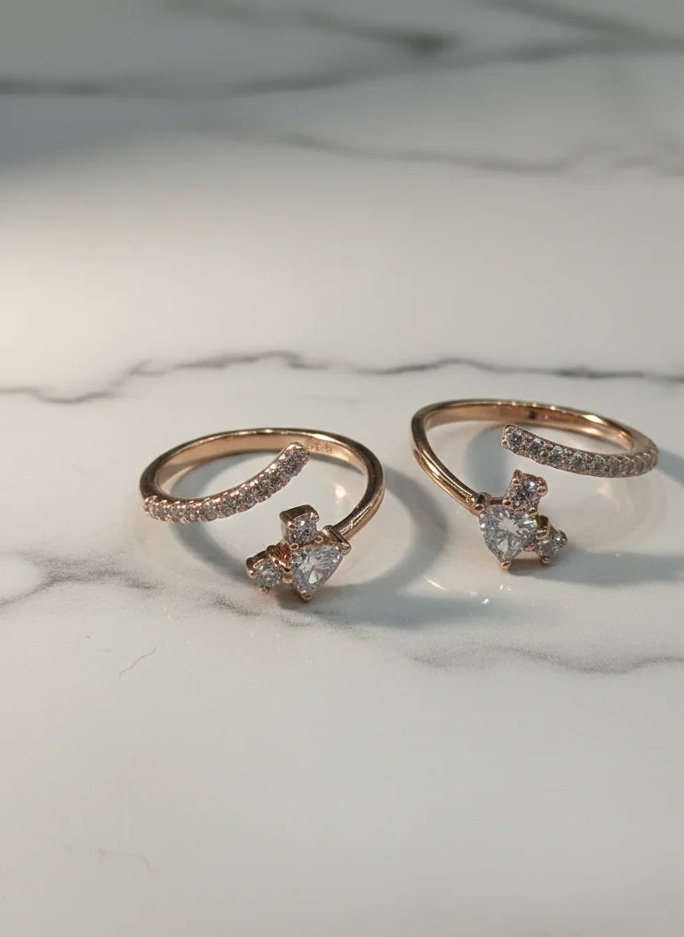 Two rose gold toe rings with heart-shaped gemstones on a marble surface
