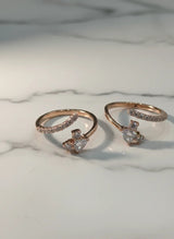 Two rose gold toe rings with heart-shaped gemstones on a marble surface