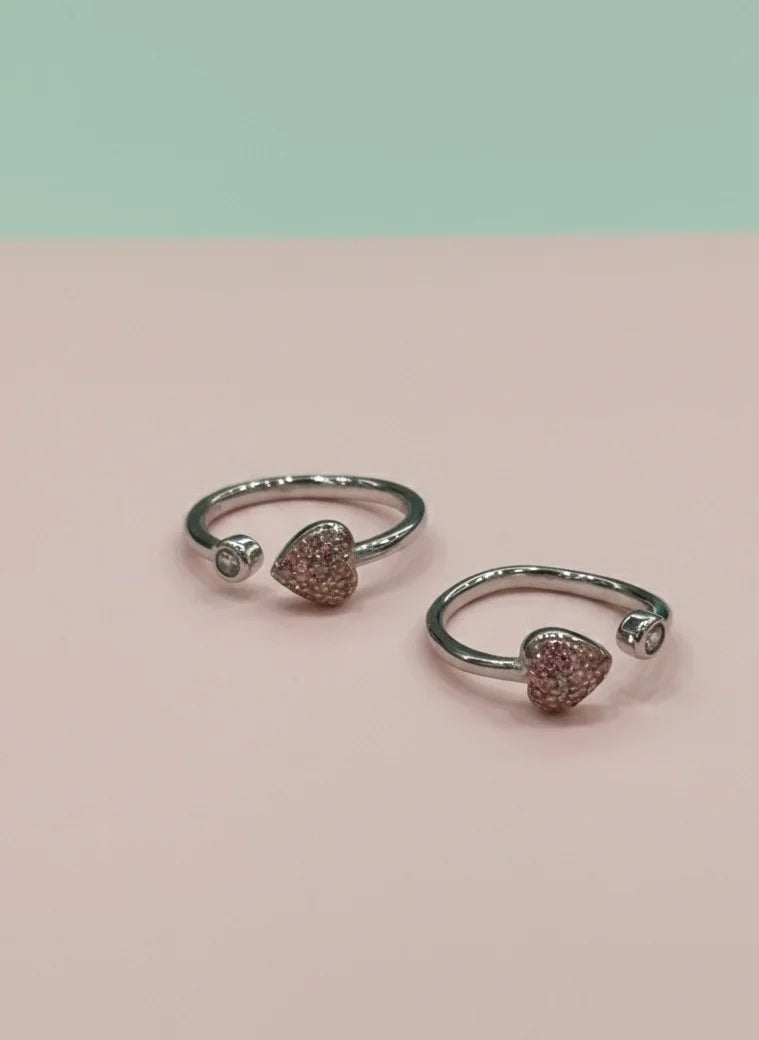 Pair of silver open toe rings with heart-shaped gemstones on a pink background