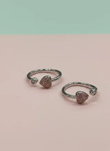 Pair of silver open toe rings with heart-shaped gemstones on a pink background