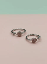 Pair of silver open toe rings with heart-shaped gemstones on a pink background