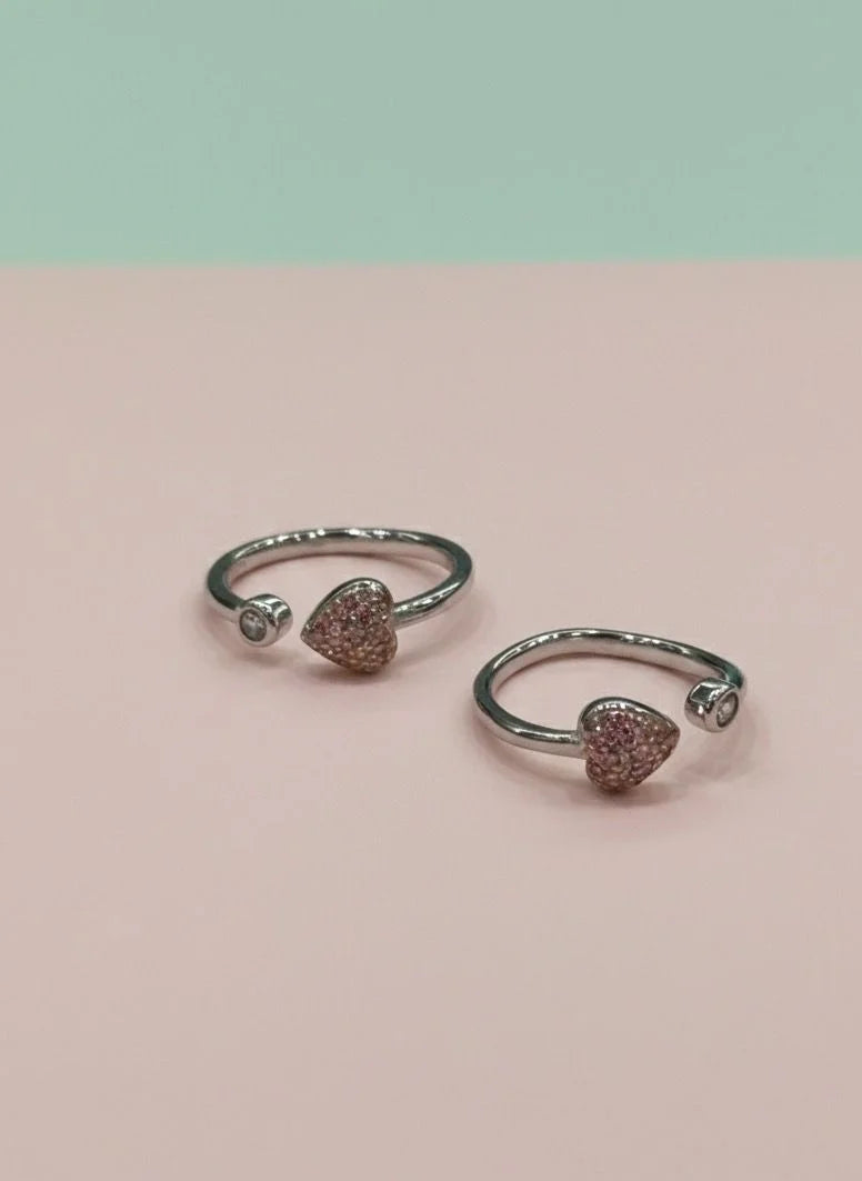 Pair of silver open toe rings with heart-shaped gemstones on a pink background
