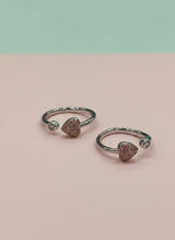 Pair of silver open toe rings with heart-shaped gemstones on a pink background