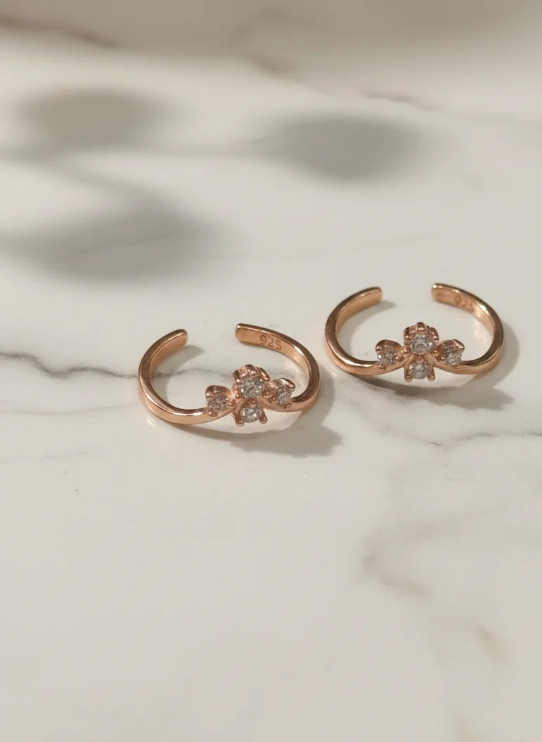 Rose gold toe rings with floral designs on a marble surface