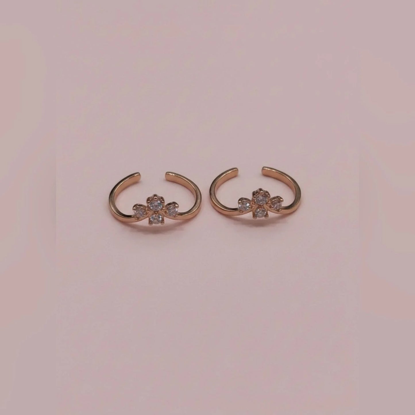 Pair of rose gold toe rings with floral designs on a pink background