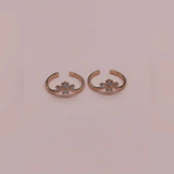 Pair of rose gold toe rings with floral designs on a pink background