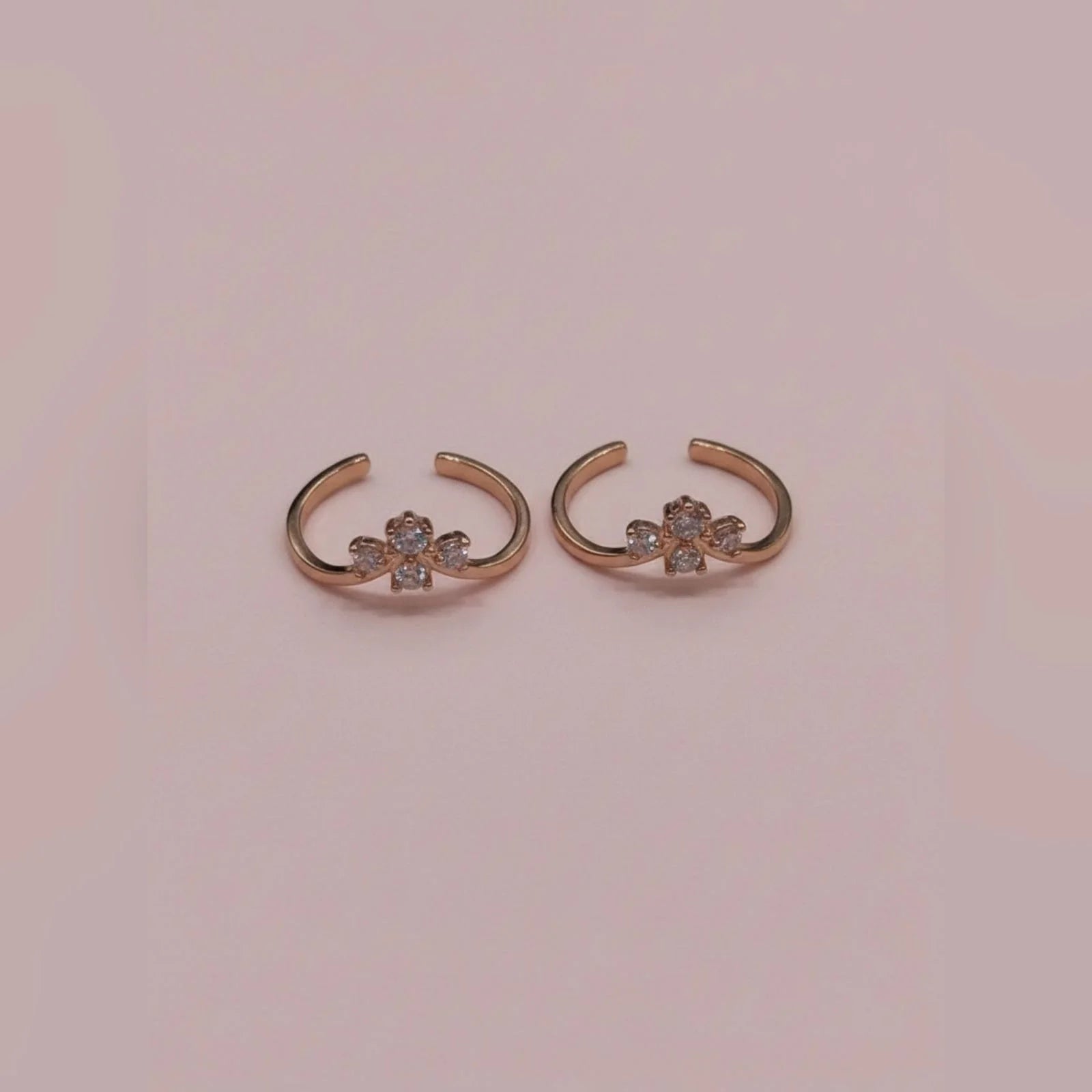 Pair of rose gold toe rings with floral designs on a pink background