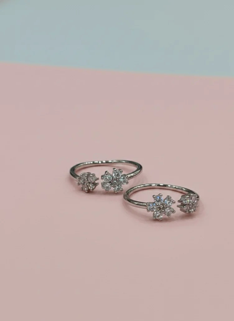 Pair of silver toe rings with floral designs on a pink and light blue gradient background