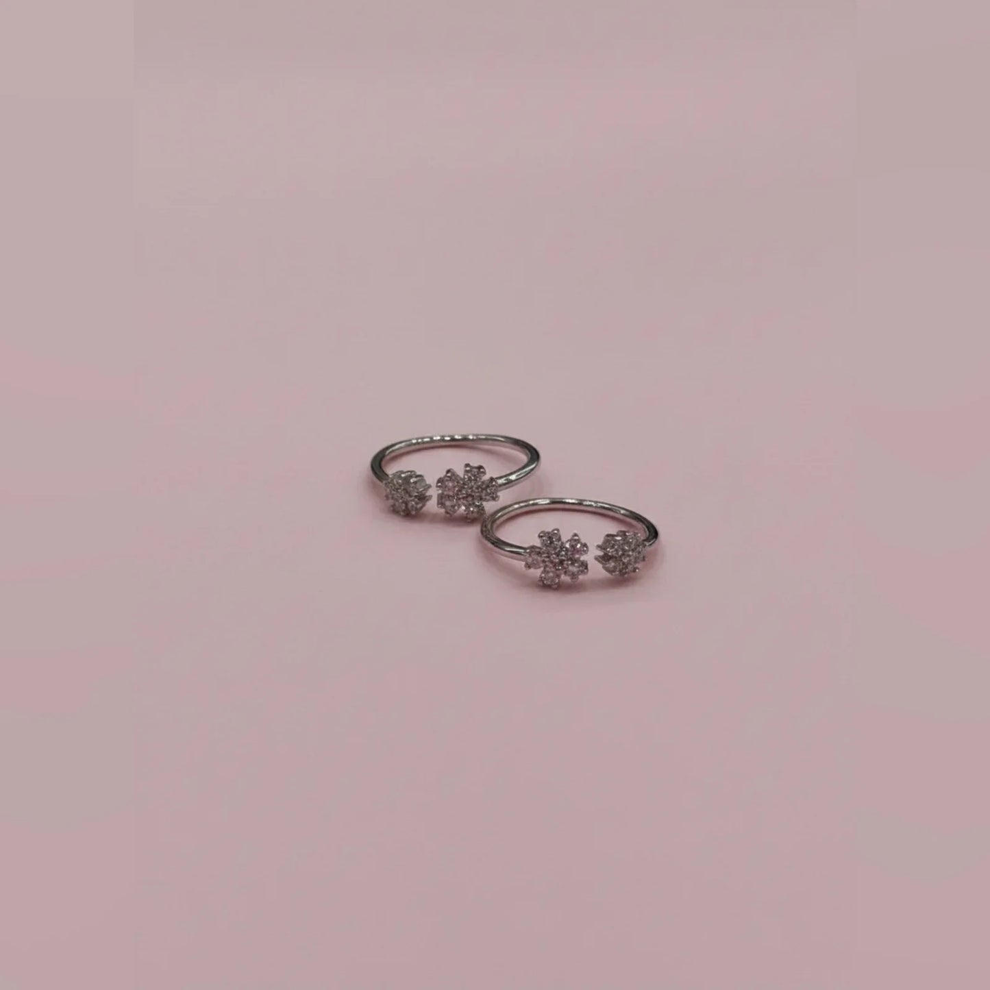 Pair of silver toe rings with floral designs on a pink background