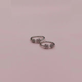 Pair of silver toe rings with floral designs on a pink background