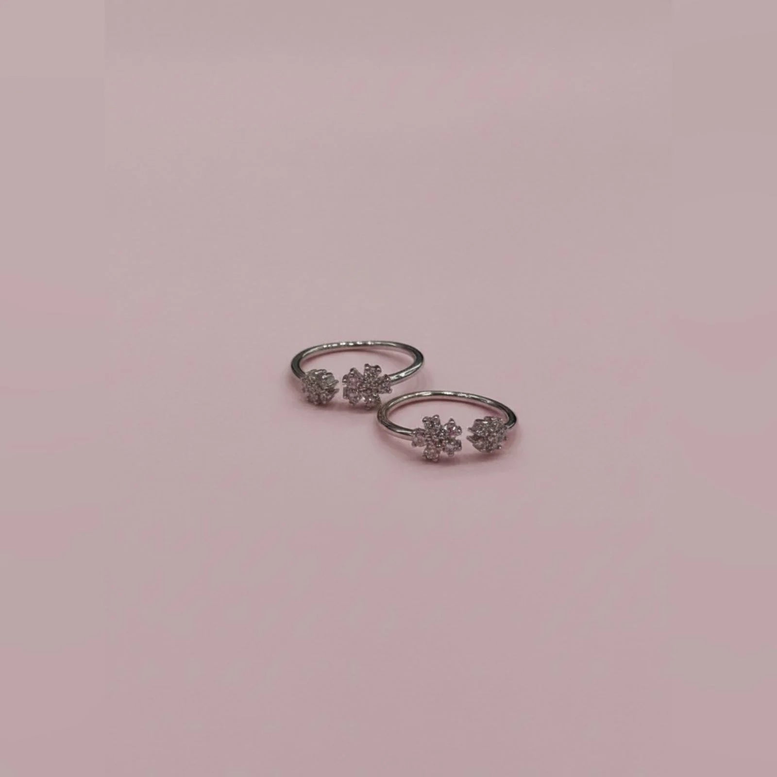 Pair of silver toe  rings with floral designs on a pink background