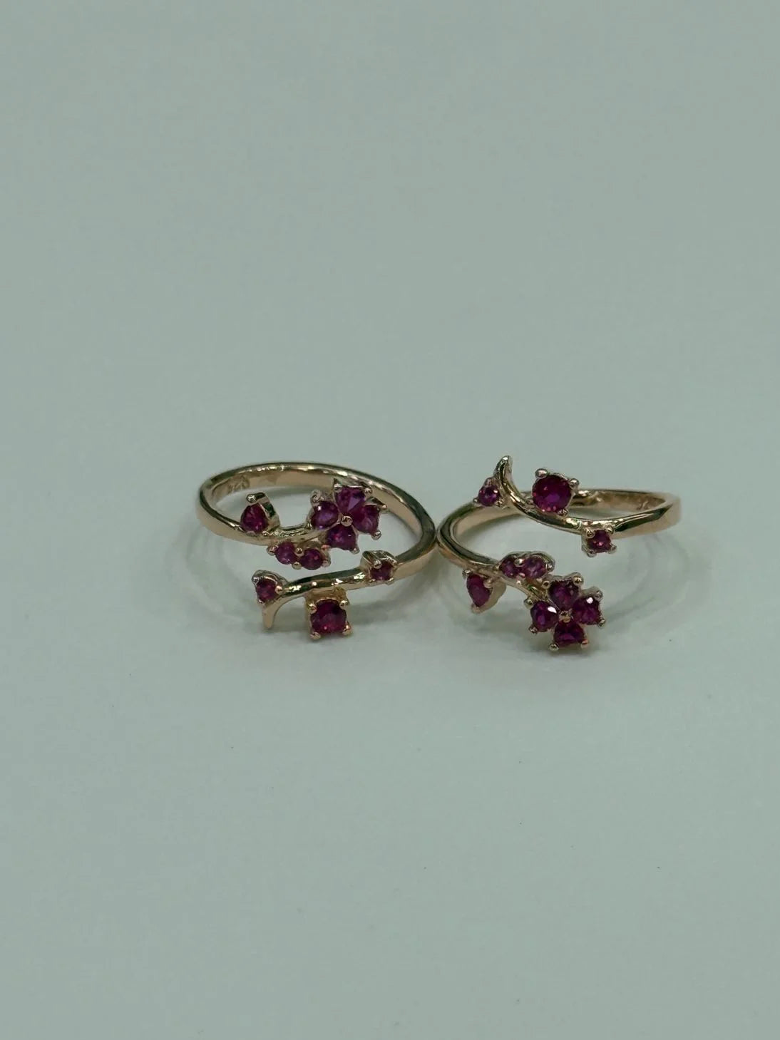 Two gold toe rings with red gemstones on a light gray background
