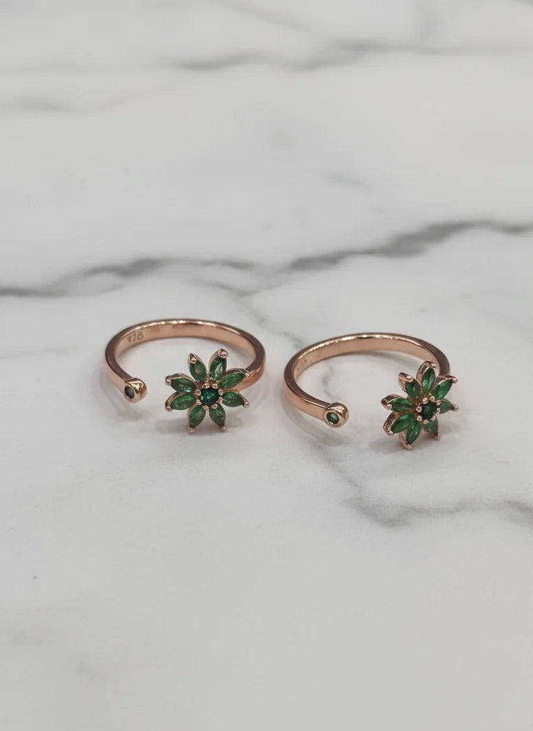 Two rose gold toe rings with green gemstones on a marble background