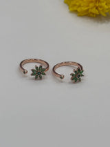 Two rose gold toe rings with green gemstones on a light gray background.