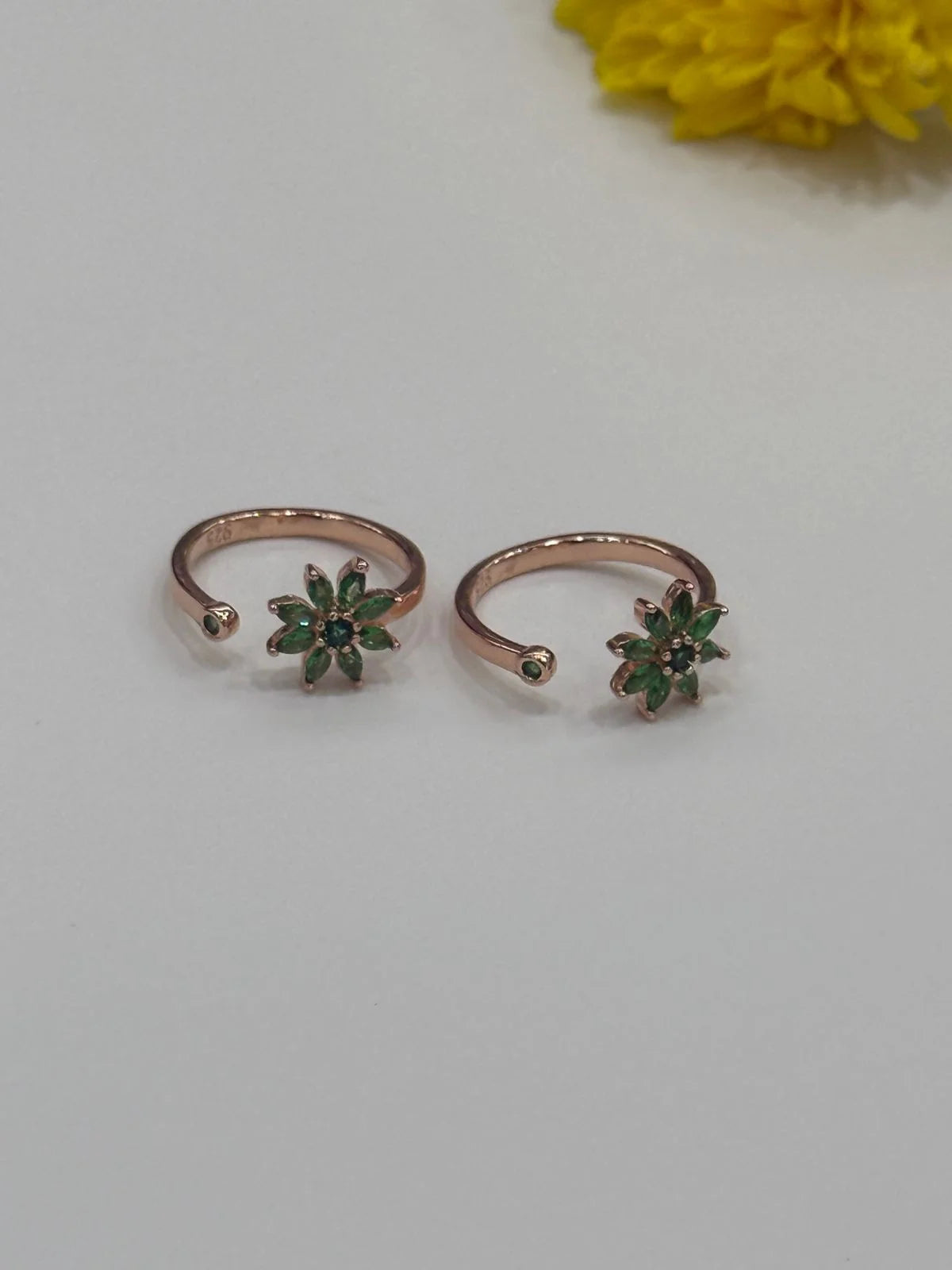 Two rose gold toe rings with green gemstones on a light gray background.