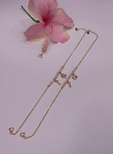 Rose gold anklet with heart-shaped pendants on a light pink background with a pink flower.