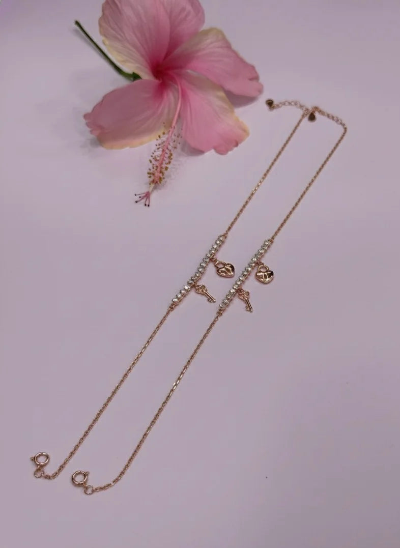 Rose gold anklet with heart-shaped pendants on a light pink background with a pink flower.