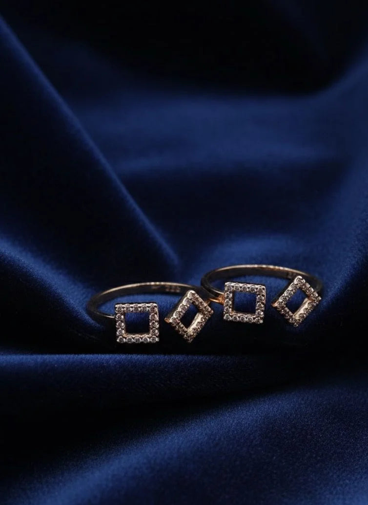 Pair of gold toe rings with square designs on a blue satin background