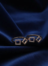 Pair of gold toe rings with square designs on a blue satin background