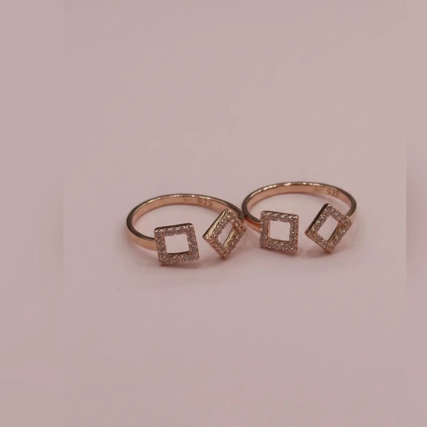 Rose gold toe ring with square-shaped gemstones on a pink background