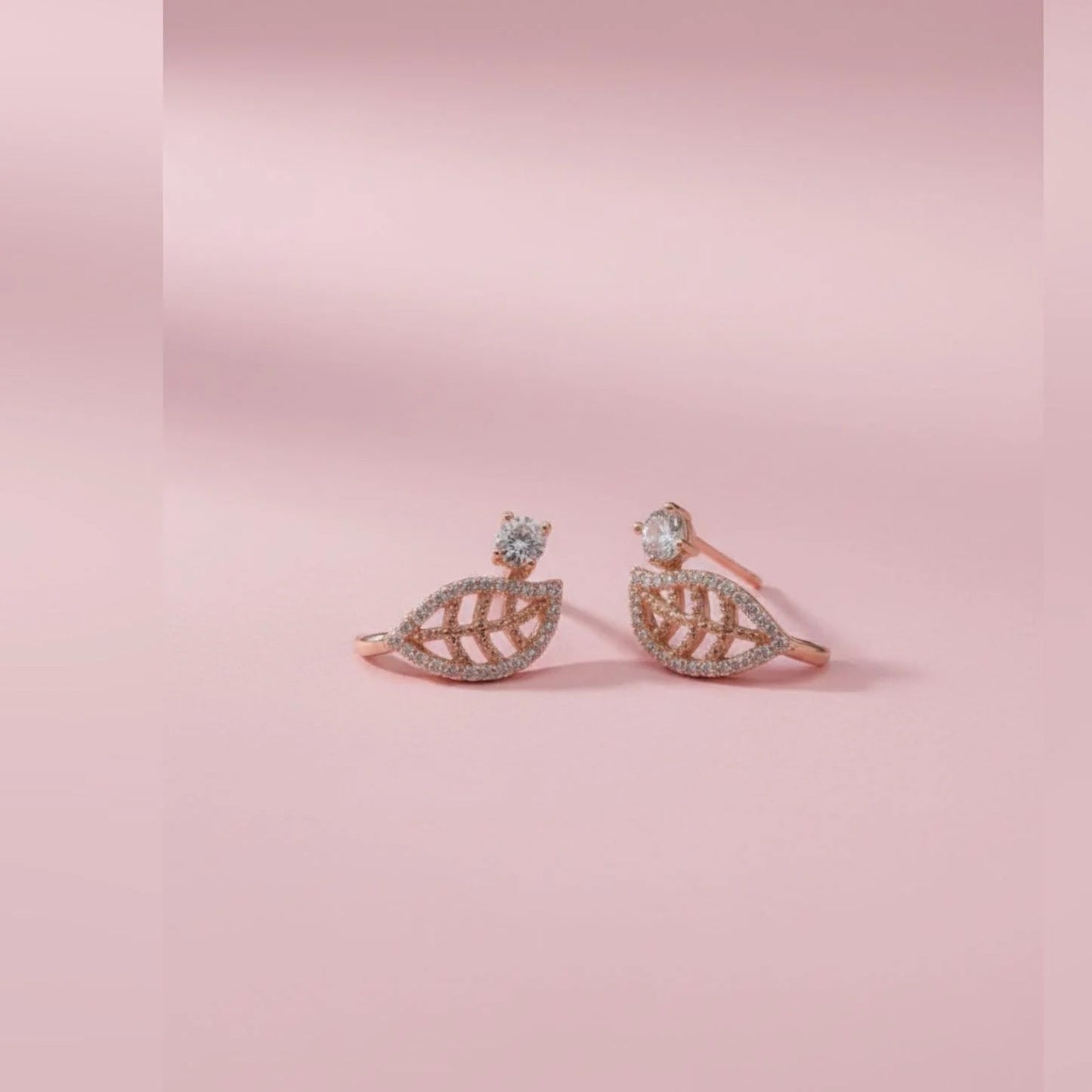 Pair of rose gold leaf-shaped toe rings on a pink background