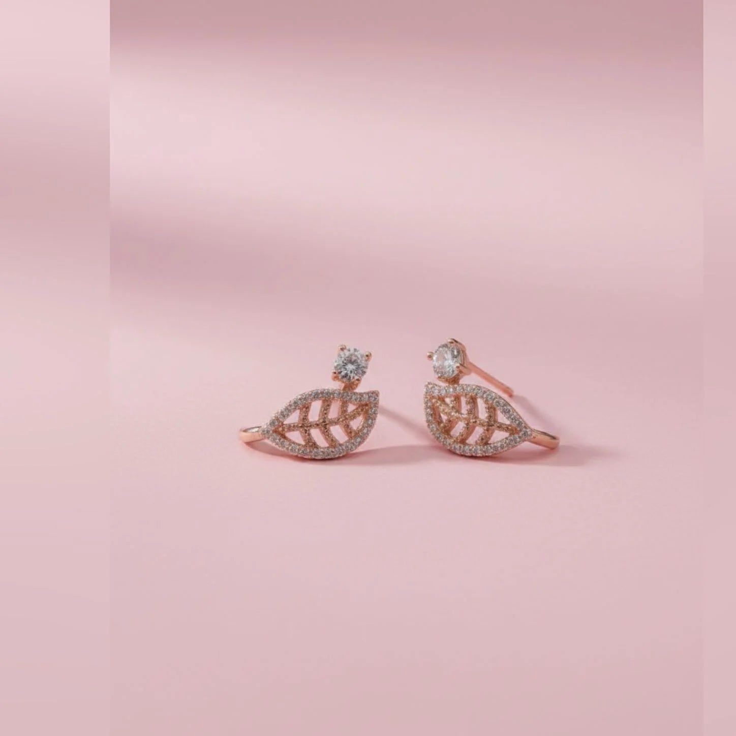 Pair of rose gold leaf-shaped toe rings on a pink background