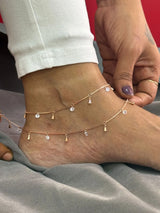 Ankle bracelet with small charms on a foot against a neutral background