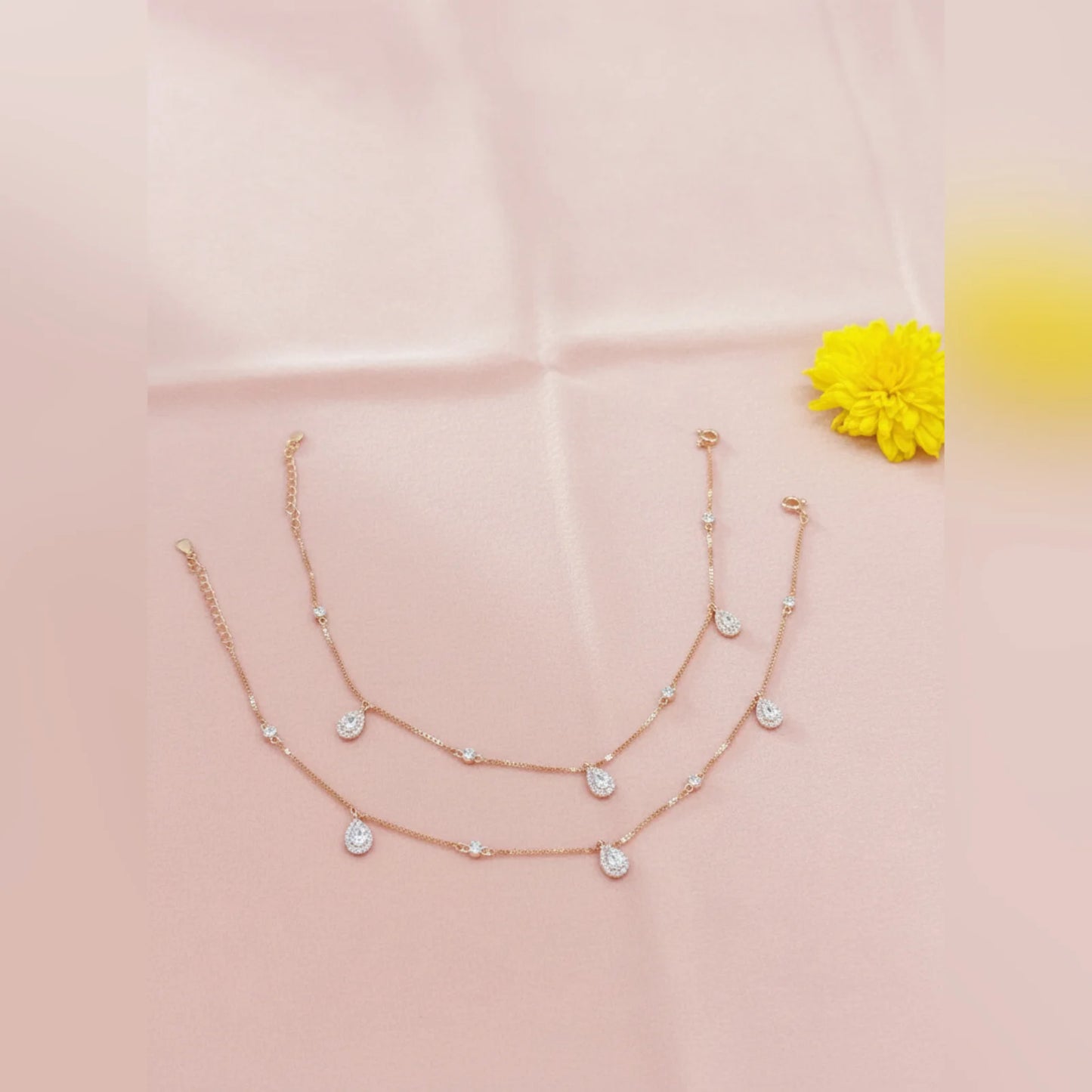Rose gold necklace with heart-shaped charms on a pink fabric background with a yellow flower.