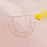 Rose gold necklace with heart-shaped charms on a pink fabric background with a yellow flower.