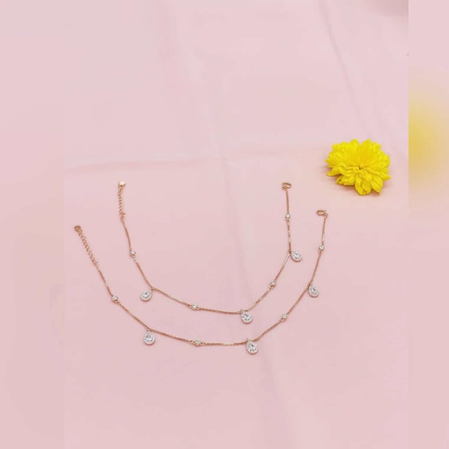 Two layered gold necklaces on a pink background with a yellow flower.