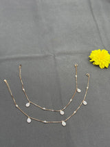 Gold necklace with teardrop pendants on a gray surface with a yellow flower.