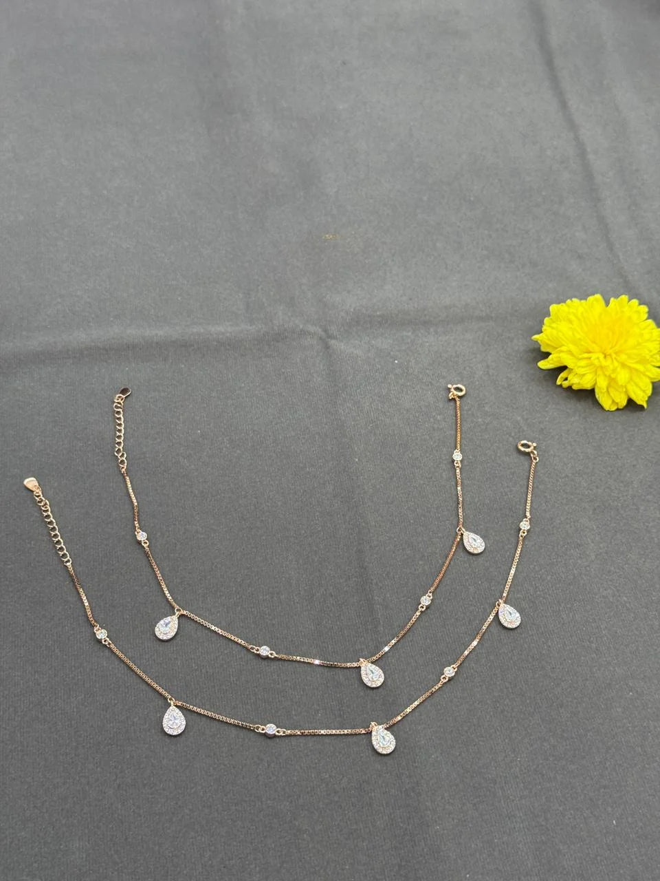 Gold necklace with teardrop pendants on a gray surface with a yellow flower.
