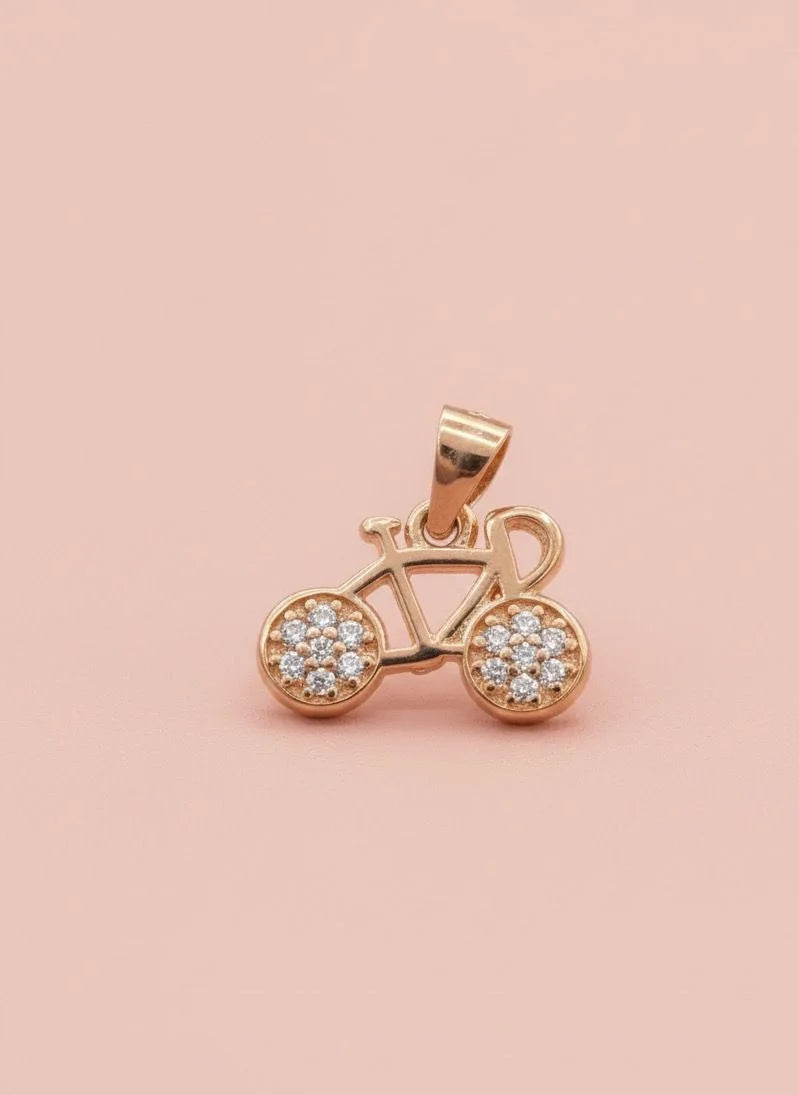 Rose gold bicycle pendant with embedded stones on a pink background