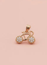Rose gold bicycle pendant with embedded stones on a pink background