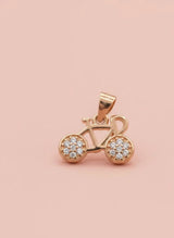 Rose gold bicycle pendant with embedded stones on a pink background