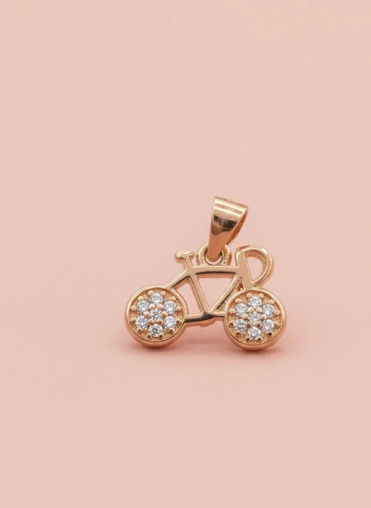 Rose gold bicycle pendant with embedded stones on a pink background