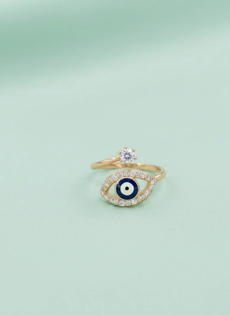 Gold ring with eye design and diamond on a light green background