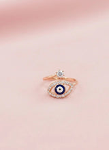 Rose gold ring with eye design on a pink background