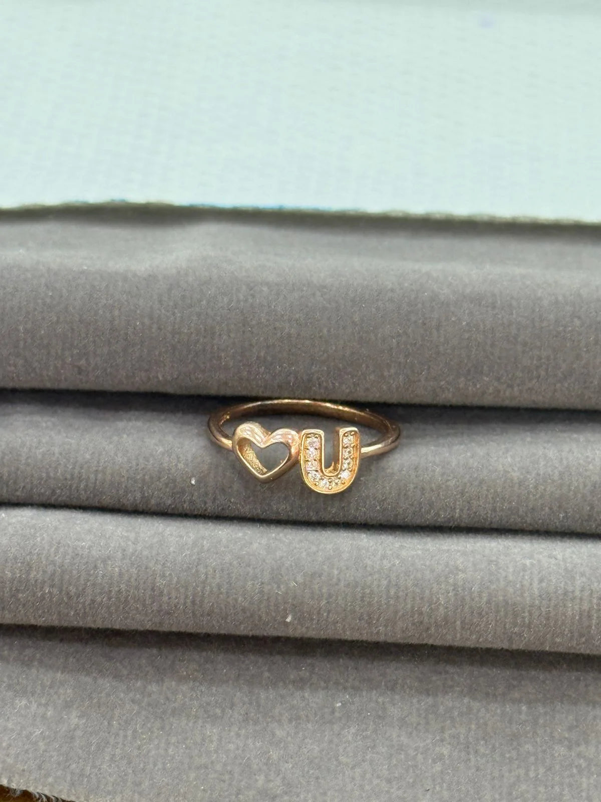Gold ring with heart and 'U' design on a gray surface