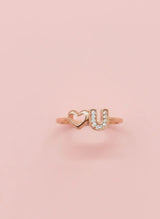 Rose gold ring with 'U' and heart design on a pink background