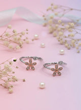 Two flower-shaped toe rings with gemstones on a pink background with small flowers.