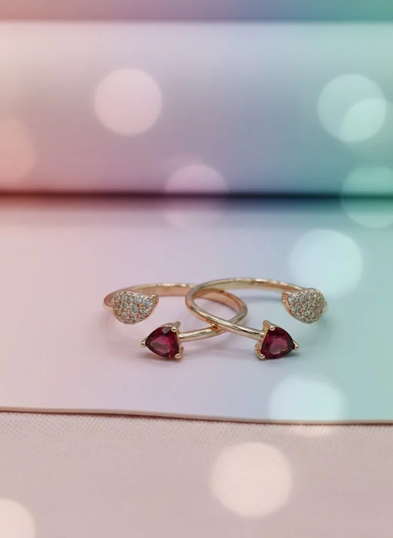 Two gold toe rings with heart-shaped gemstones on a blurred background