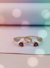 Two gold toe rings with heart-shaped gemstones on a blurred background