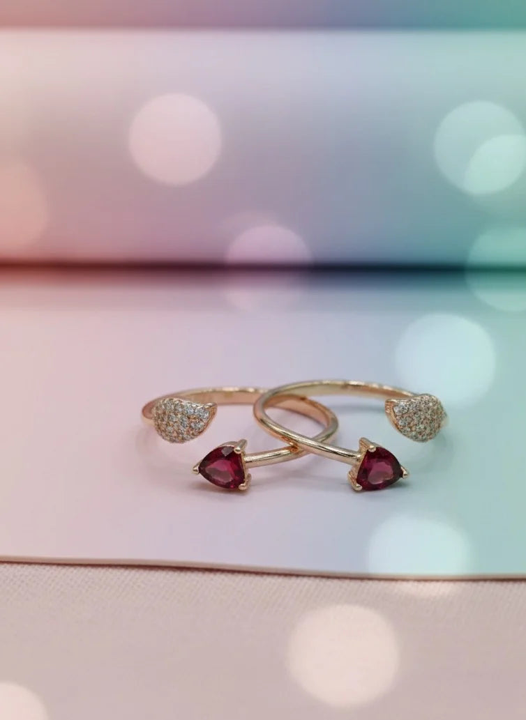 Two gold toe rings with heart-shaped gemstones on a blurred background