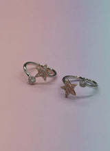 Two star-shaped toe rings with gemstones on a gradient background