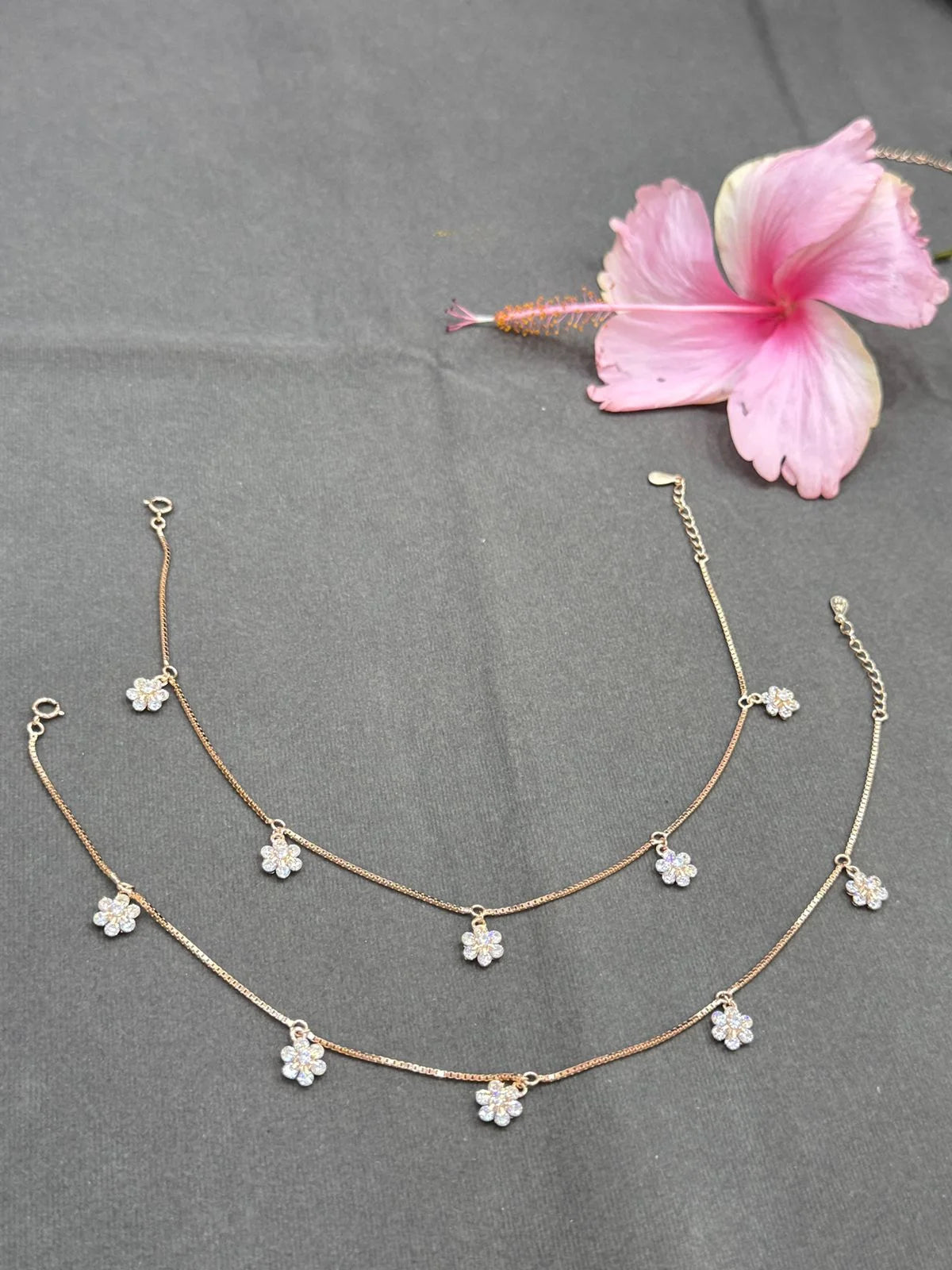 Anklet with floral pendants on a gray surface with a pink flower.