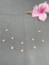 Two gold anklet  with floral pendants on a gray surface with a pink flower.