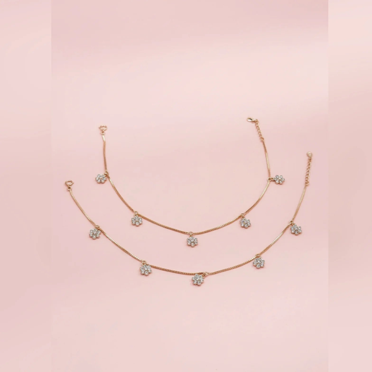 Rose gold anklet with diamond-like stones on a pink background