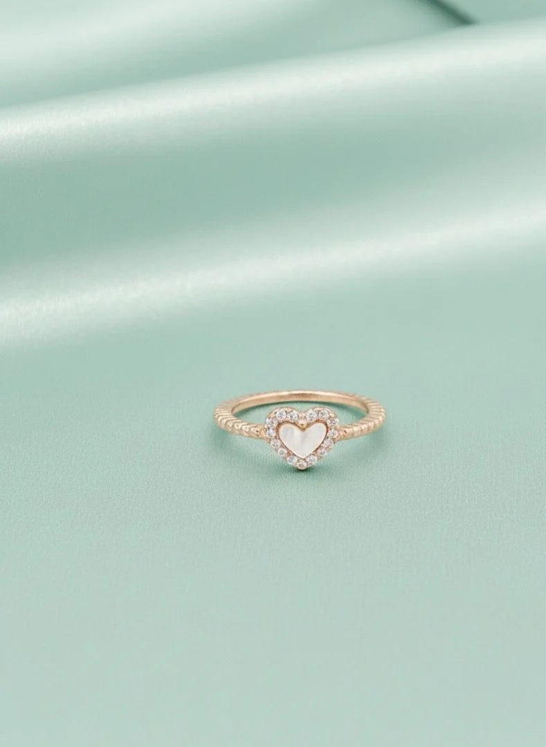 Rose gold ring with a heart-shaped center on a light green background