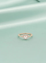 Rose gold ring with a heart-shaped center on a light green background